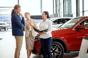 Smiling couple considering a red SUV while speaking with a car saleswoman inside a dealership showroom