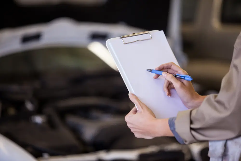 An appraiser holding a clipboard and pen while inspecting a vehicle's engine bay, capturing critical details during the vehicle evaluation process.