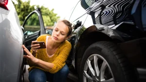Woman crouched near a car taking a photo of a dent or scratch after a parking lot accident