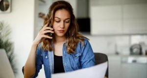 Woman at home on phone while reviewing insurance documents after a car accident