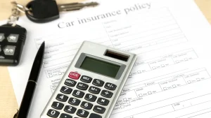 Car insurance form with a calculator, pen, and car keys on a desk