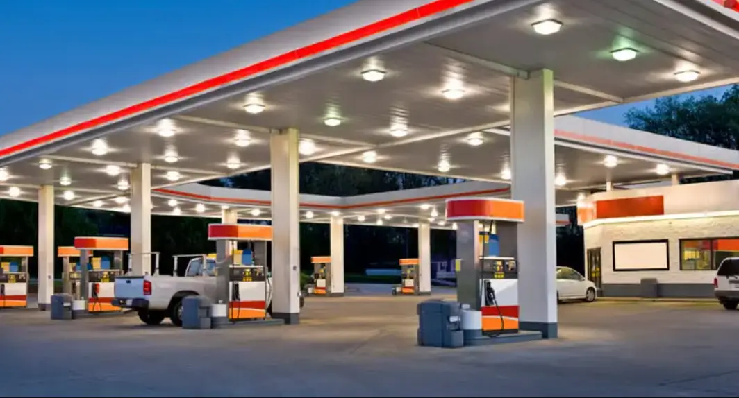 A brightly lit gas station with multiple fuel pumps, a white truck, and cars under the canopy at dusk.