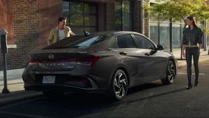 A Hyundai Elantra Hybrid parked on a city street, with two people standing nearby, showcasing its elegant design and eco-friendly performance.