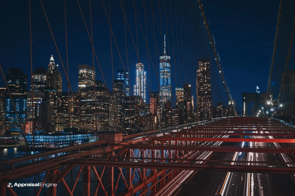 Night view of traffic streaking across the Brooklyn Bridge with the illuminated New York City skyline in the background.