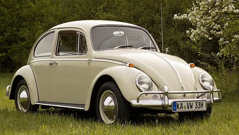 An iconic Volkswagen Beetle, representing the early success of the brand, parked on a grassy field with lush greenery and blooming trees in the background.