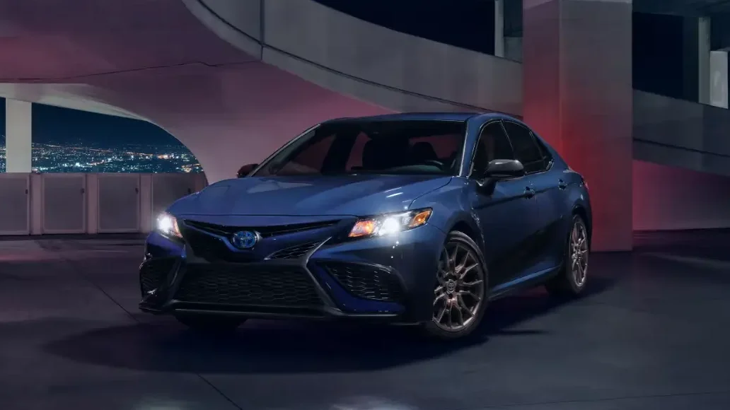 A sleek blue Toyota Camry Hybrid parked in an urban setting at night, exemplifying economic and fuel-efficient cars in a stylish design.