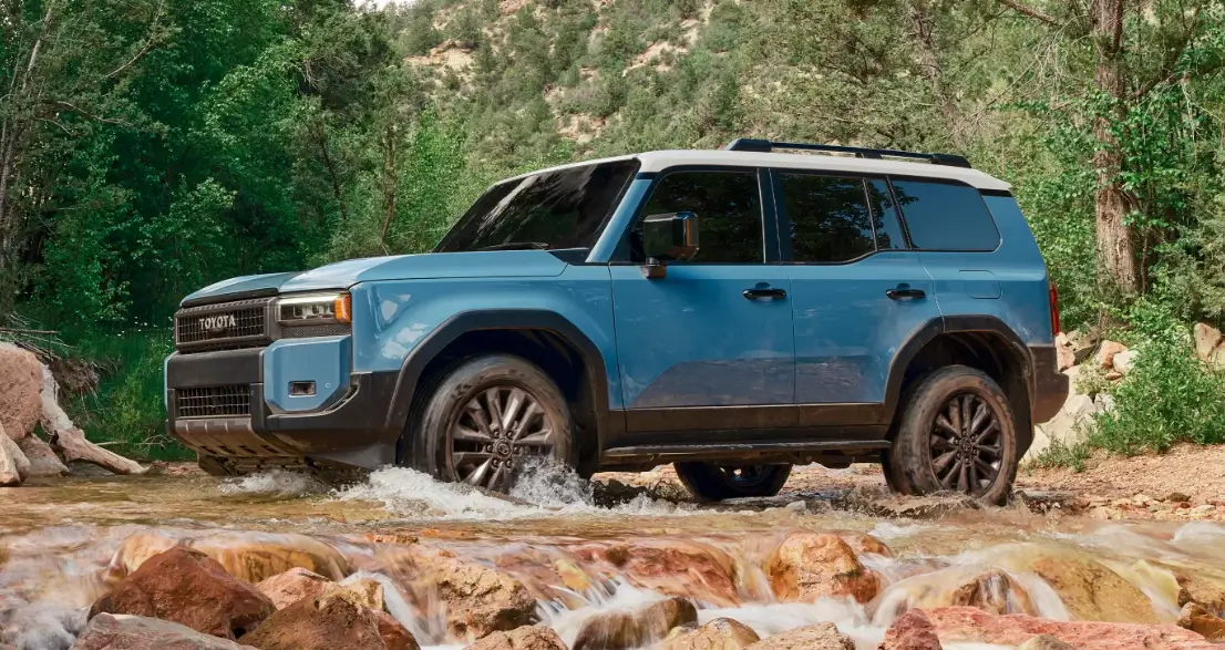 Blue Toyota SUV crossing a shallow stream in a forested area, showcasing the vehicle's off-road capabilities and rugged design.