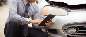 Insurance adjuster using a tablet to assess front-end damage on a car during an AI insurance claim valuation