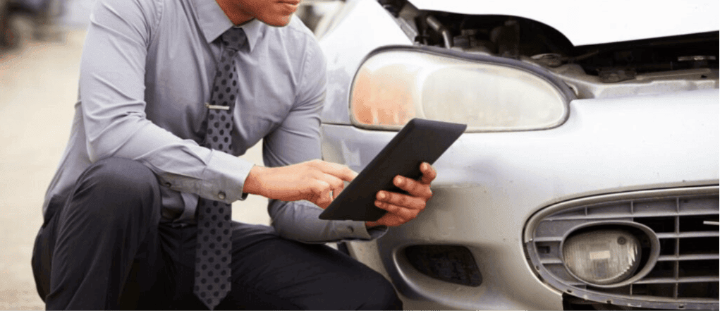 Insurance adjuster using a tablet to assess front-end damage on a car during an AI insurance claim valuation
