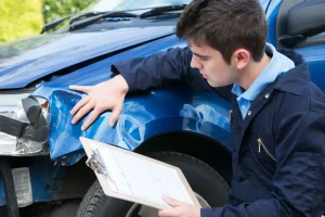 Auto appraiser inspecting damage on a blue vehicle with clipboard in hand.