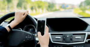 Driver holding smartphone while driving, illustrating distracted driving behavior that leads to accidents and vehicle value loss