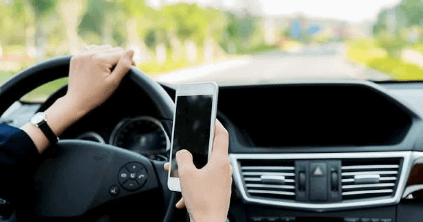 Driver holding smartphone while driving, illustrating distracted driving behavior that leads to accidents and vehicle value loss