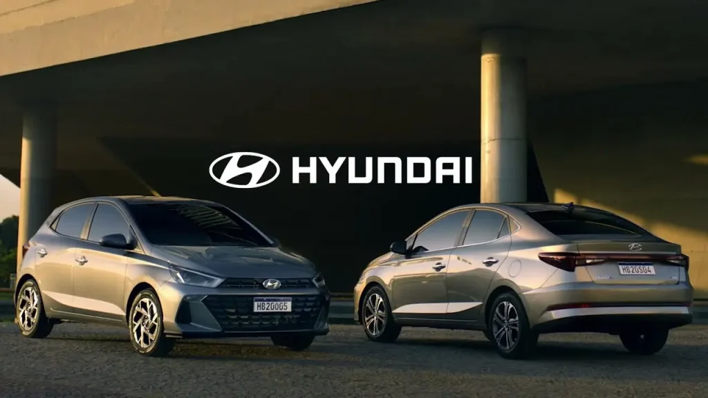 Two modern Hyundai cars, a hatchback and a sedan, are parked under a concrete structure with the Hyundai logo prominently displayed above them, representing Hyundai's evolution in automotive design and innovation.