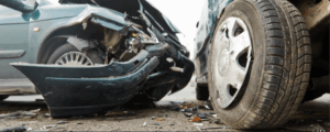 Close-up of two cars with severe front-end collision damage showing crushed bumper and debris on the road