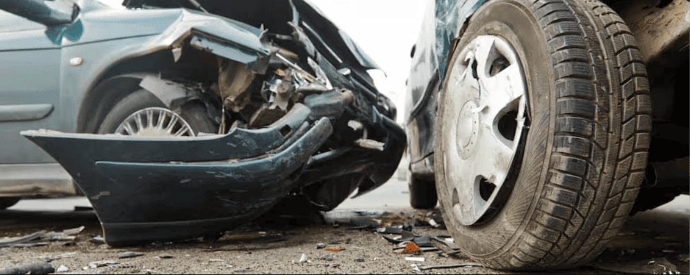Close-up of two cars with severe front-end collision damage showing crushed bumper and debris on the road