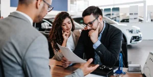 Couple reviewing paperwork with a car dealer inside a dealership.