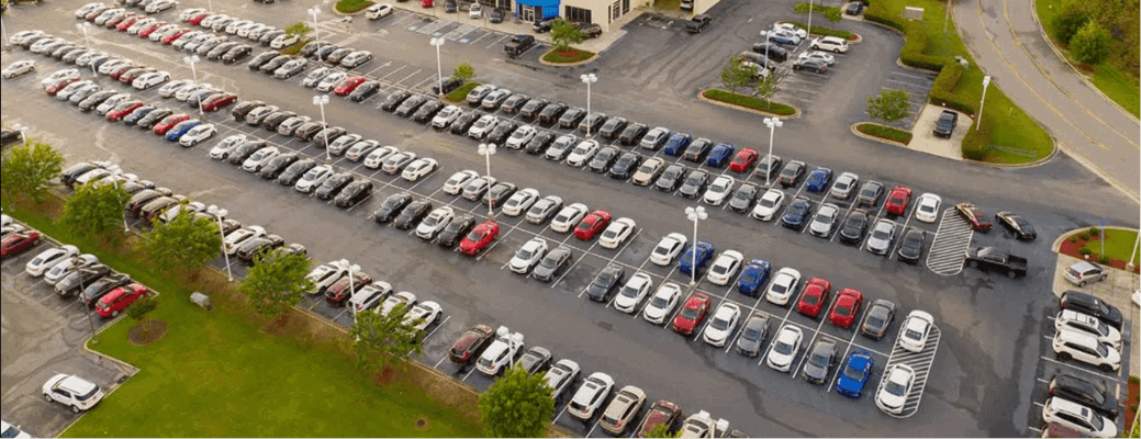 Aerial view of a car dealership parking lot filled with rows of new vehicles illustrating vehicle affordability challenges